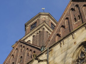 A pointed brick church tower with decorative details and clock under a bright blue sky, Coesfeld,