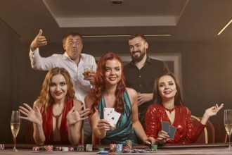 Happy friends are playing poker at casino. They are celebrating their win, smiling and posing at