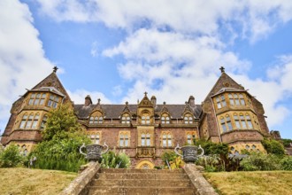 Large building with symmetrical architecture, surrounded by garden and staircase under blue sky.