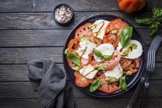 Italian caprese salad with sliced tomatoes, mozzarella cheese, basil, olive oil. Served on black