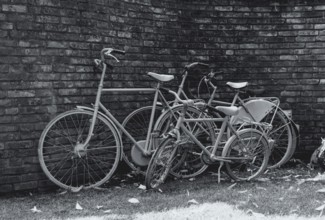 Three bikes grass in front of a stone wall in black and white in the netherlands