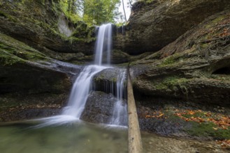 A waterfall flows over moss-covered rocks in a secluded forest, covered with autumn leaves,
