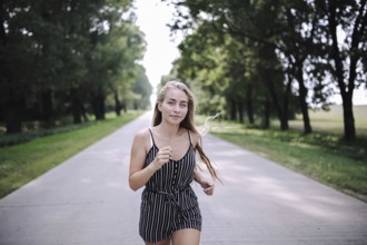 Woman running on a tree-lined road during a sunny day