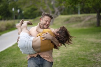 Man with happy expression carrying his girlfriend in his arms in a park