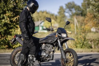 Biker in black helmet standing by an off-road bike in the countryside