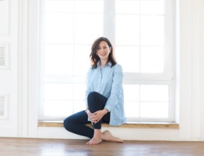 Young brunette woman sitting by the window smiling at the camera