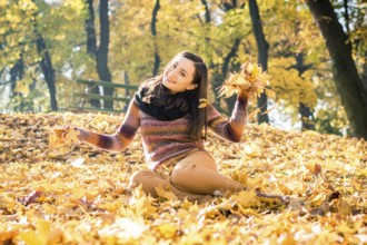 Beautiful girl in autumn Park keeps yellow leaves