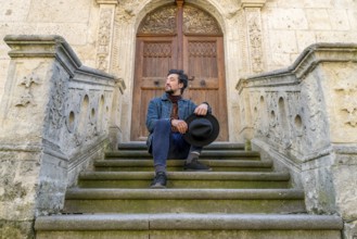 Portrait of a young man sitting against a beautiful old medieval cathedral door. A man in front of