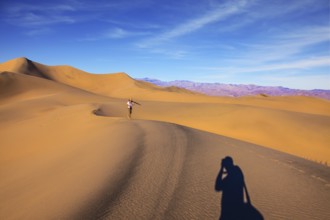 Orange sand dunes in Death Valley, California. A middle-aged woman in striped T-shirt carries a