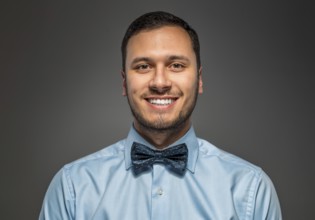 Portrait of happy smiling young man in blue shirt and butterfly tie isolated over gray studio