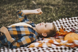 Kid boy lies near a river, pond or lake and smiling. Autumn season. Happy childhood