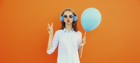 Portrait of happy cheerful young woman in wireless headphones listening to music with balloon on