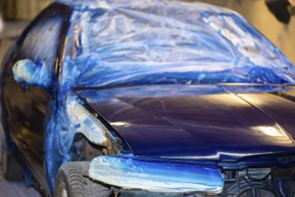A blue car partially covered with plastic sheeting in a workshop setting