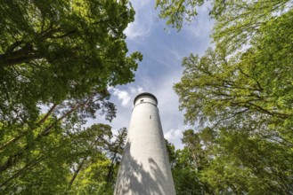 A white observation tower in a park, surrounded by green trees and a small seating area in summer,