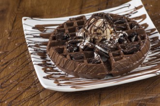 Wafer cake in a square white plate on a wooden lacquered surface with reflection