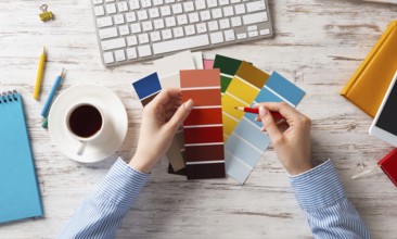 Web designer choosing colors from swatches at wooden desk. Office workplace with computer keyboard
