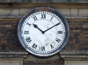 Old round clock on the brick wall of a building with roman numerals with hands at ten past ten
