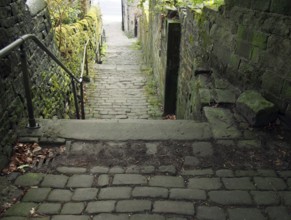 Old outdoor stone steps in dark alley with cobblestones and moss growing on the walls