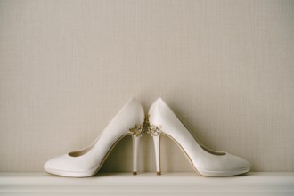 White women's shoes with high pointed heels, with a pattern of flowers, on a gray background.