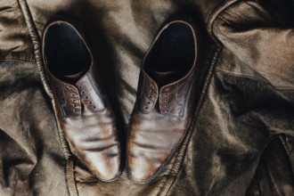 Brown leather shoes placed on a rustic jacket, exuding a vintage and worn aesthetic