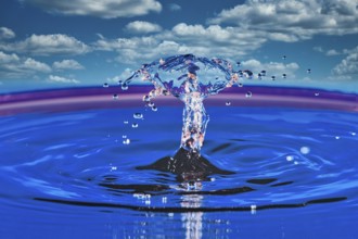 A splashing drop of water in front of a blue sky with white clouds, highspeed photography, drop