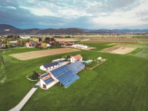 Aerial view of a small farm with roof tops covered in solar panels. Cloudy day in spring