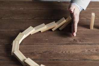 Businesswoman protecting dominoes from falling on wooden desk. Business assistance and leadership