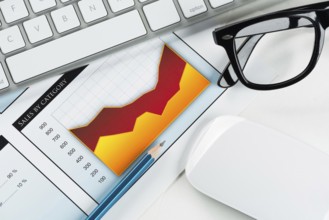 Business workplace with keyboard glasses and financial documents on table