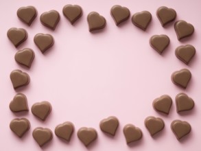 Frame of romantic chocolate confections in heart shapes on pastel pink background. Canvas with