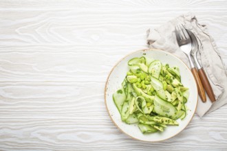 Healthy vegan green avocado salad bowl with sliced cucumbers, edamame beans, olive oil and herbs on