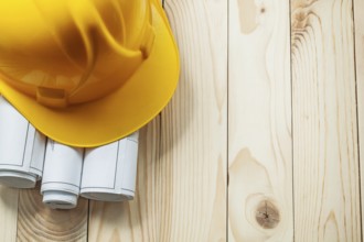 Yellow construction helmet and white rolled blueprints on wooden boards