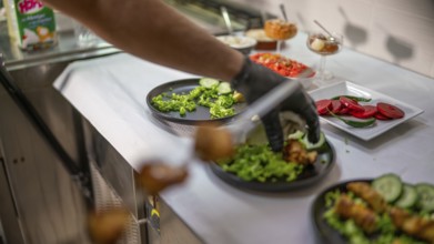 Chef wearing black gloves is garnishing plates with fresh vegetables and sauces, preparing various