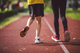 Close-up of the legs in trainers of two children on the running track in the stadium, back view.