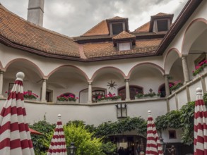 Historic courtyard with arcades, balconies, red and white umbrellas and many plants, Dürnstein,