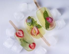 Popsicles with lemon balm and strawberries and ice cubes on a white background