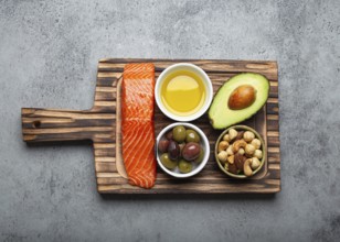 Food sources of healthy unsaturated fat: fresh raw salmon fillet, avocado, olives, nuts on cutting