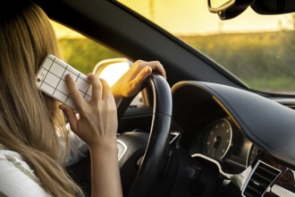 Young woman using mobile phone while driving car on highway road during sunset. Womandriver has