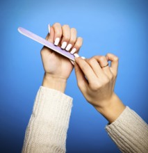 Faceless female in sweater filing long white nails doing manicure on blue background