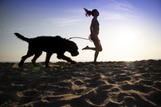 Girl running in the company of her dog on the seashore shot against the light