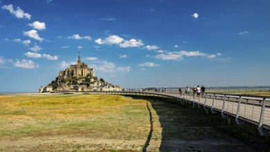 Mont Saint-Michel in summer with a pedestrian bridge in the foreground and blue sky, Mont Saint