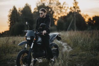Man sits on a motorcycle on a nature path at sunset, embodying tranquility