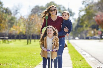 Mother daughter and son family in the park walking with ball and skate scooter