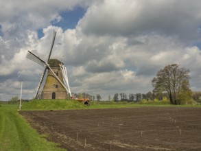 Windmill on a hill next to a freshly ploughed field and green meadow under a blue sky, Eibergen,