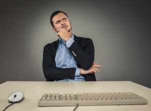 Handsome man in blue shirt and jacket looking up, sitting at a desk near a computer, isolated on
