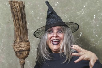 Old witch with white hair and a black hat with an ancient broom in her hands and a terrifying