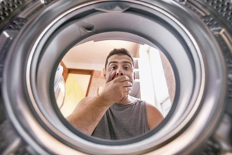 Shocked upset Young man Looking At Stained Bleached Cloth In Washing Machine. View from the inside