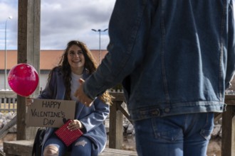 Young woman with a happy valentine's day sign, a balloon of hearts and a red gift, giving a