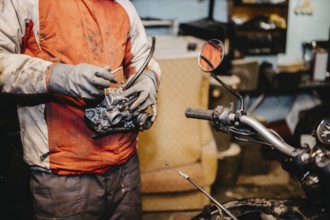 Mechanic inspecting motorcycle part in a workshop with a motorbike nearby
