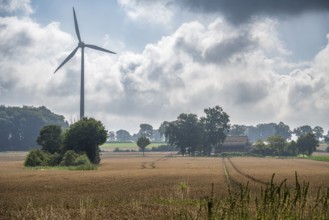 Rural landscape with wind turbine and fields under a slightly cloudy sky, wind turbine and farm in