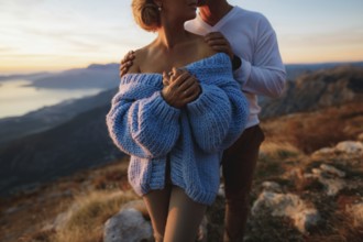 Man hugs a woman in a blue sweater by the shoulders on the background of mountains. Close up.